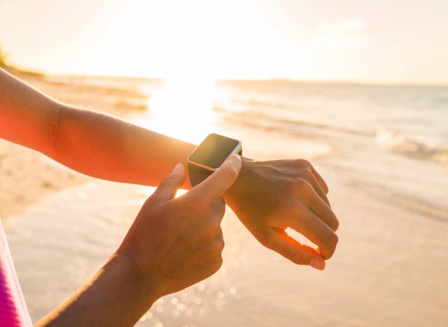 woman checking fitness tracker on beach at sunset