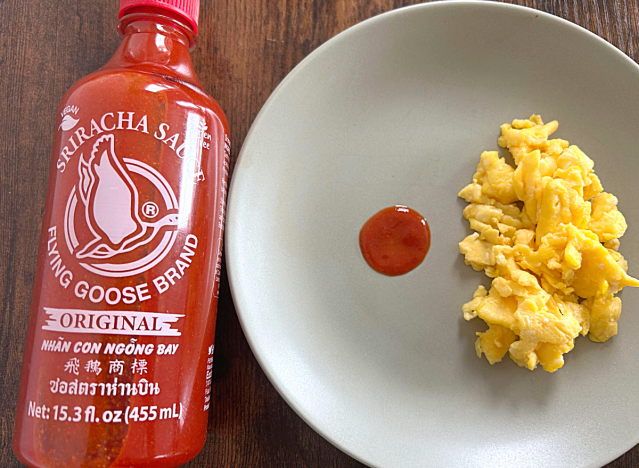 a bottle of flying goose sriracha next to a plate of eggs with a dollop of sriracha 