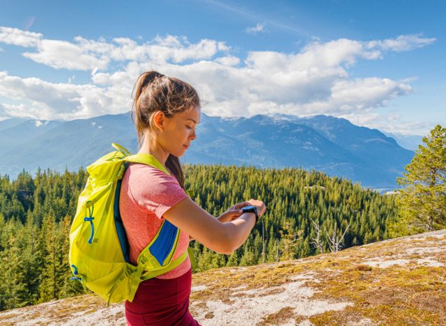 female hiker wearing rucksack at top of mountain looking at watch