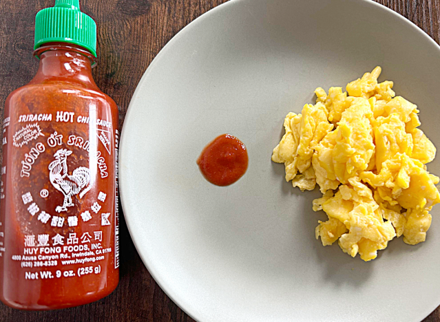 a bottle of huy fong sriracha next to a plate of eggs and a dollop of sriracha 