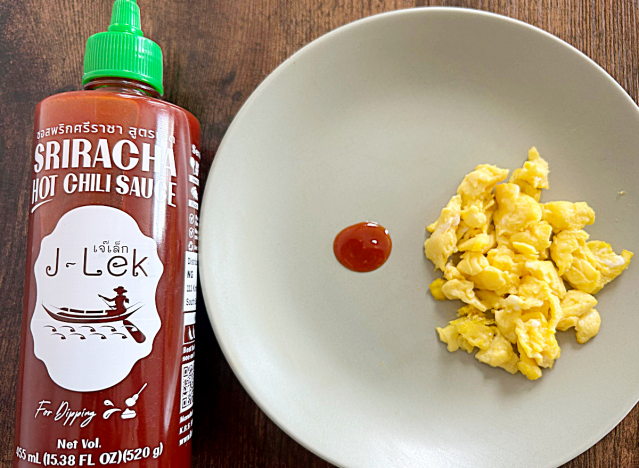 a bottle of j-lek sriracha next to a plate of eggs and a dollop of sriracha 