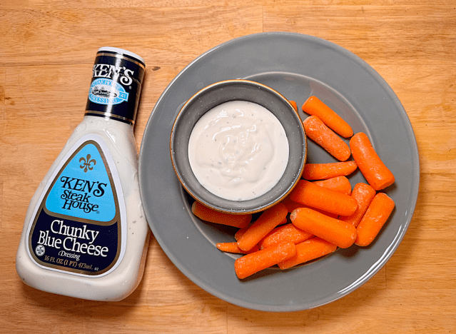 a bottle of blue cheese from ken's next to a plate of carrots 