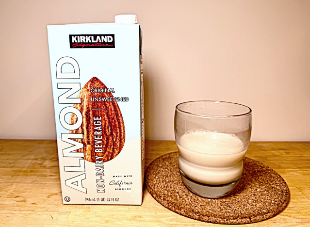 a container of kirkland almond milk next to a glass 