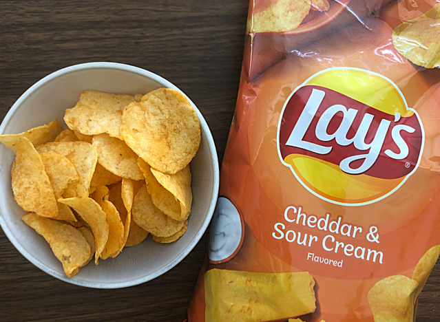 a bag of lays cheddar sour cream next to a bowl of chips