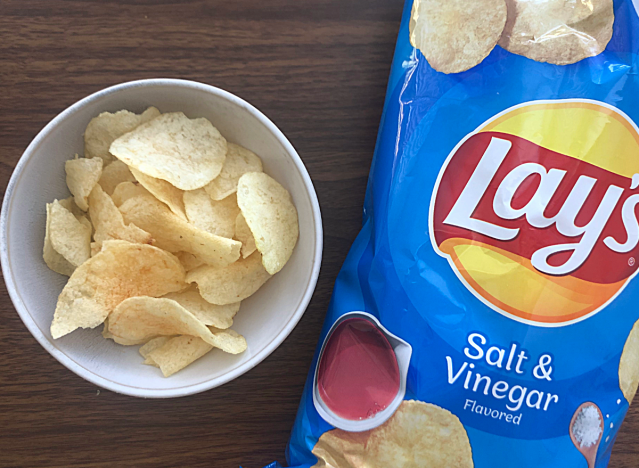 a bag of lays salt and vinegar chips next to a bowl of chips