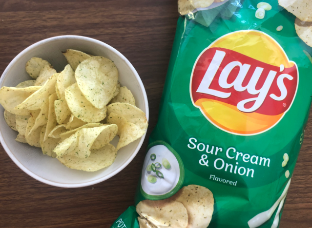 a bag of lays sour cream and onion next to a bowl of chips