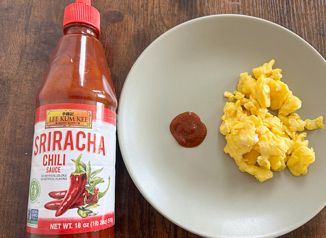 a bottle of lee kum kee sriracha next to a plate of eggs and a dollop of sriracha 