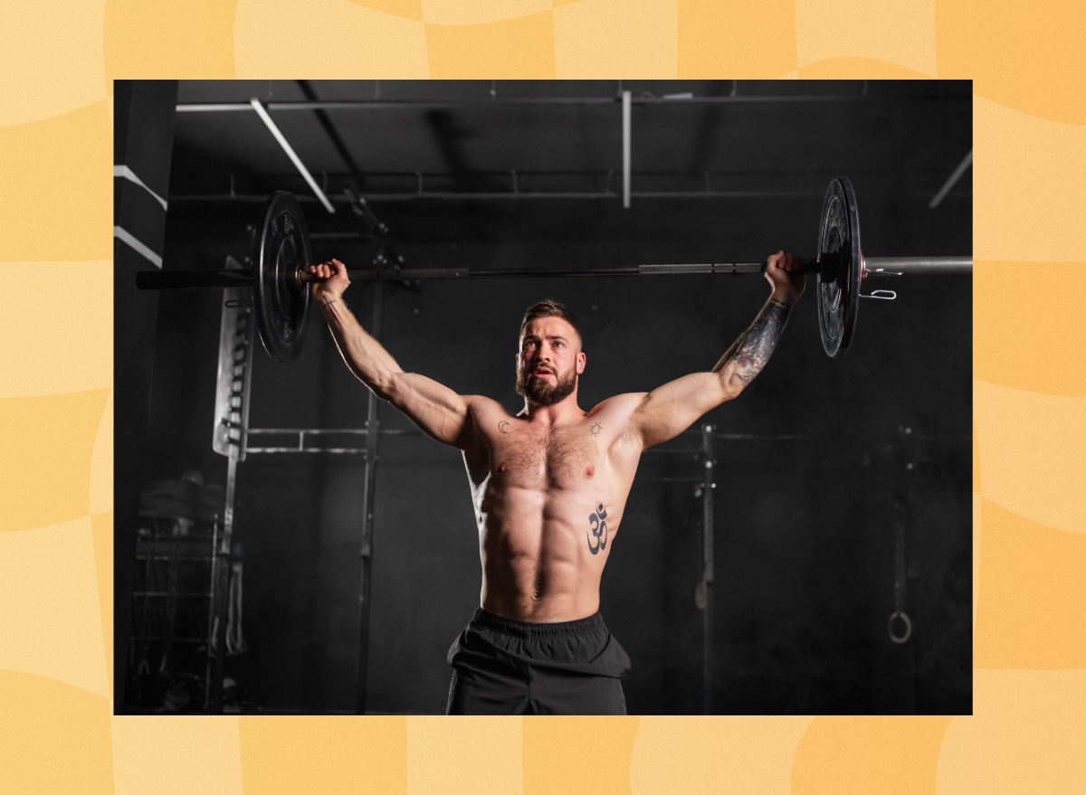 muscular man doing a barbell overhead press in a dark gym