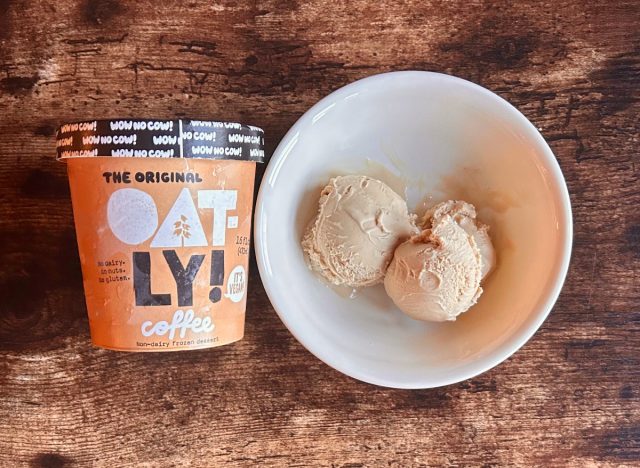 a pint of oatly's coffee-flavored frozen dessert next to a bowl of coffee frozen dessert on a wooden table background