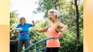 happy senior woman hula hooping outdoors with friend on sunny day in park