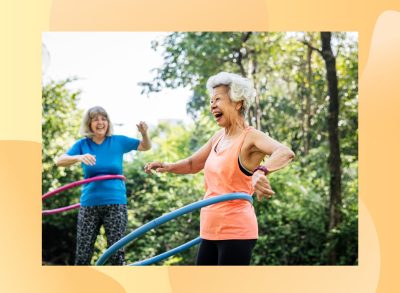 happy senior woman hula hooping outdoors with friend on sunny day in park