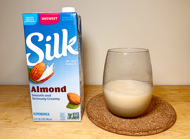 a container of silk almond milk next to a glass of it 