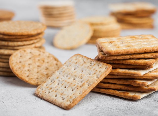 Stack of various organic crispy wheat, rye and corn flatbread crackers with sesame and salt on light background