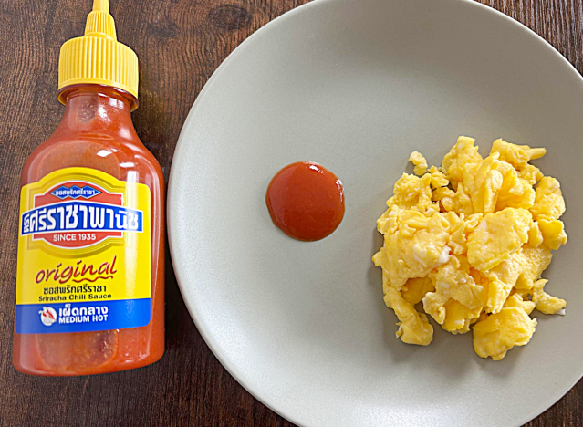a bottle of sriracha next to a plate of eggs with a dollop of sriracha 