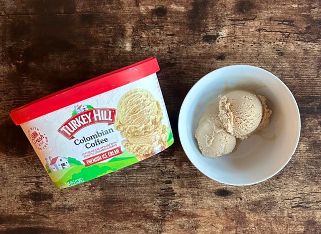 a container of turkey hill's coffee ice cream next to a bowl of coffee frozen dessert on a wooden table background