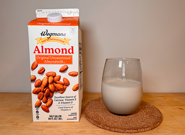 a container of wegman's almond milk next to a glass of it 