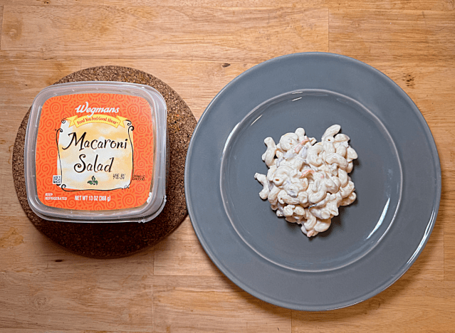 a container of wegman's macaroni salad next to a plate of it 