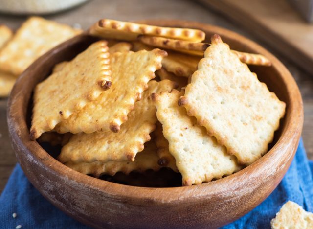 Homemade thin crispy cheesy crackers with sesame seeds in rustic wooden bowl - fresh organic homemade baking cheese crackers snack