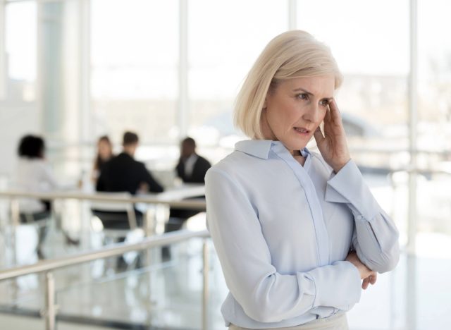 mature woman standing outside work meeting, finding it difficult to concentrate