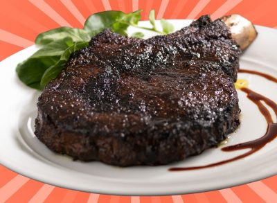 A porcini-rubbed ribeye steak with balsamic vinegar on a white plate, set against a vibrant orangish pink background.
