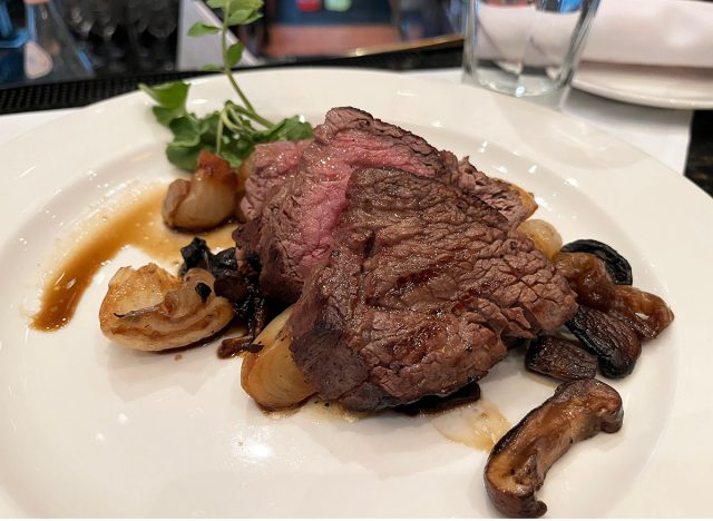 Sliced filet mignon with cipollini onions on a white plate at Capital Grille in NYC