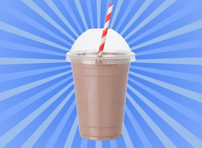 A chocolate milkshake in a clear plastic cup with a striped straw set against a vibrant blue background