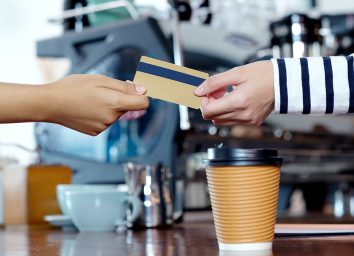 Close up of customer hand holding credit, debit electronic card to buy coffee by at cafe shop counter