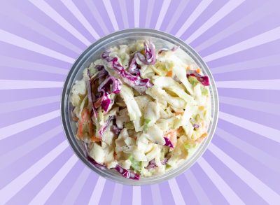 A closeup view from above of an open coleslaw container set against a vibrant purple background.