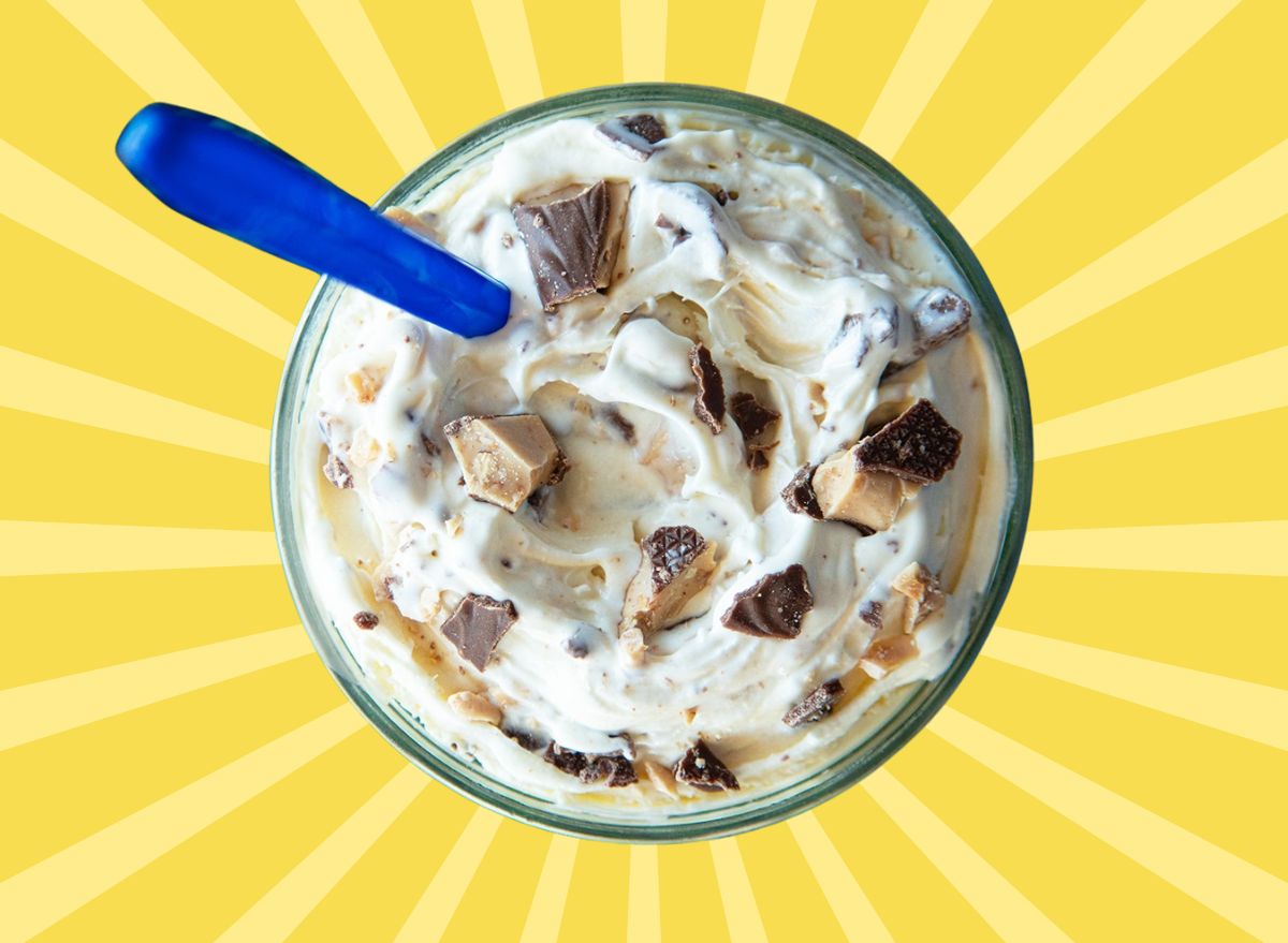 A closeup of a frozen custard concrete, mixed with candy bar pieces and set against a vibrant yellow background.