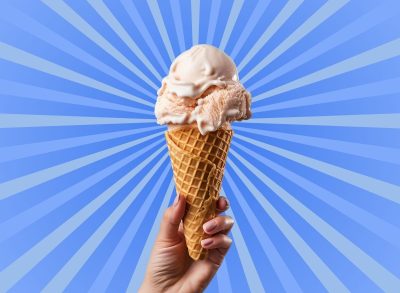 Hand holding ice cream cone in front of striped blue background