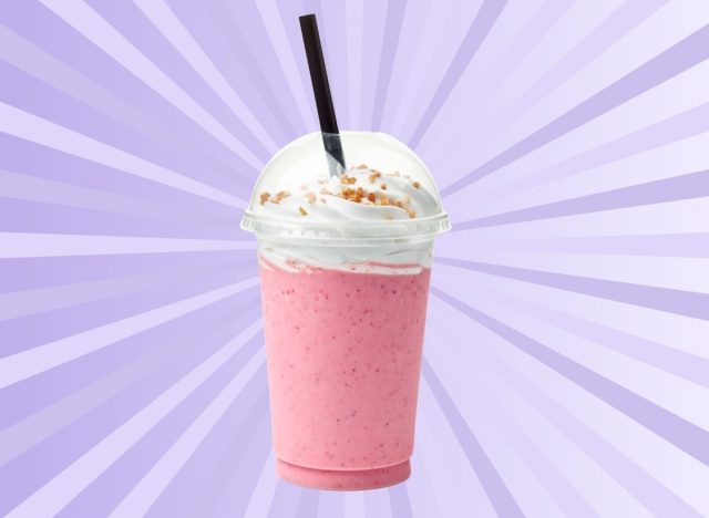 A pink-colored strawberry milkshake with whipped cream and a straw set against a vibrant purple background