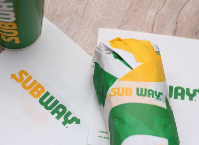 Subway wrapped sandwich, napkins, and drink on table