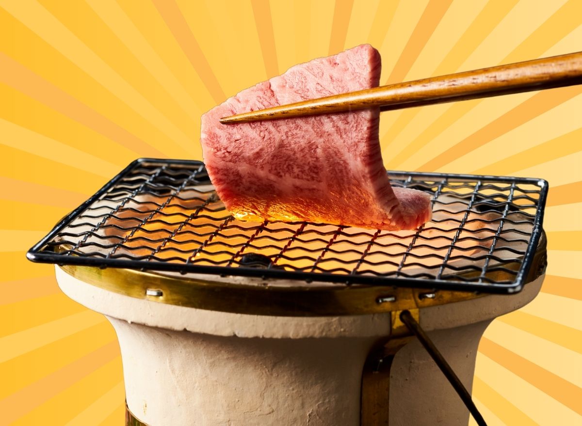 A pair of chopsticks holding a slice of Wagyu beef over a hot grate