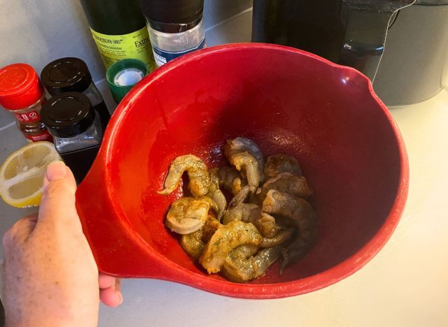 red bowl of raw shrimp in front of an air fryer