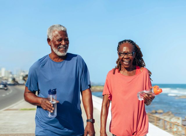 happy mature couple laughing and walking for exercise by the beach