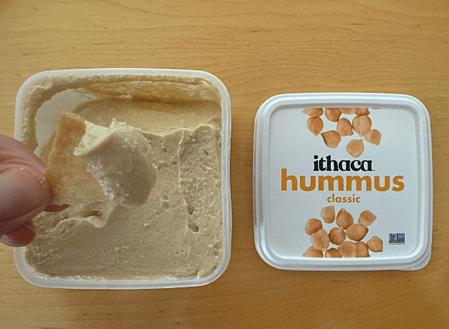 ithaca hummus container open with chip being dipped into it 