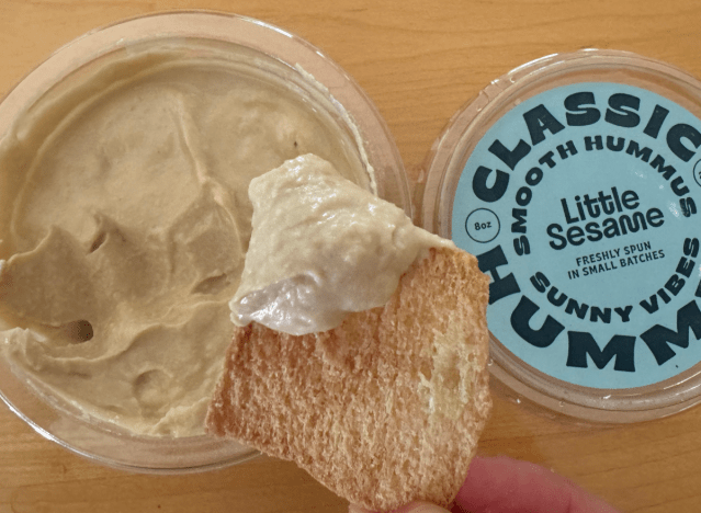 little sesame hummus container open with chip being dipped into it 