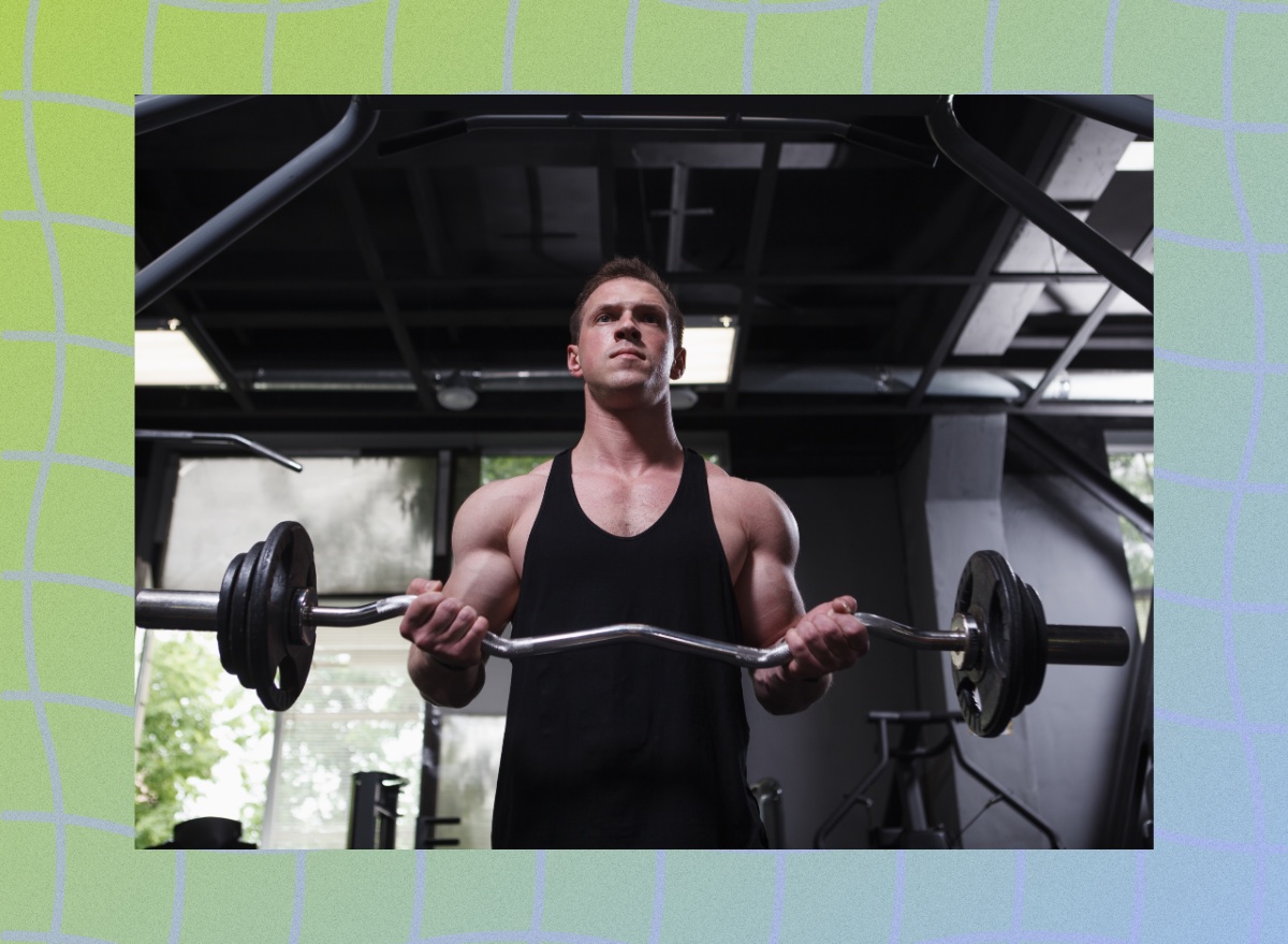 focused muscular man doing EZ bar curls at the gym in dark weight room