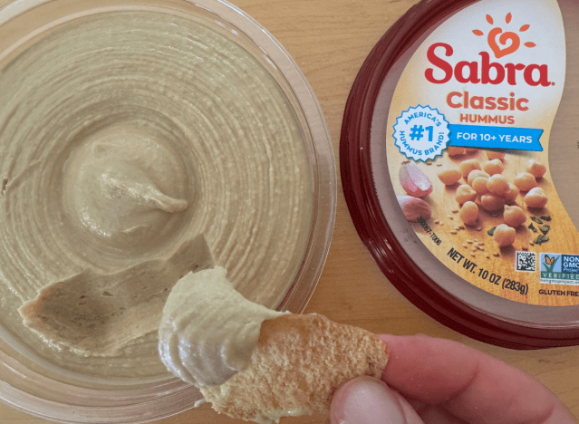 sabra hummus container open with chip being dipped into it 