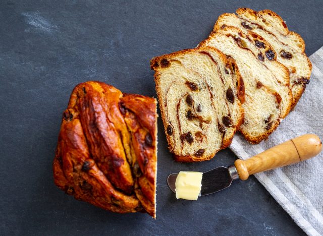 Homemade raisin and cinnamon bread on a gray slate slab with a linen cloth and pat of butter on a knife