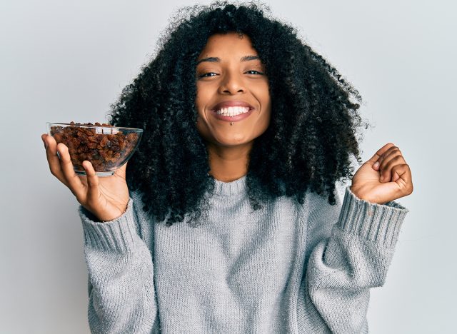 African american woman with afro hair holding raisins in bowl screaming proud, celebrating victory and success very excited with raised arm