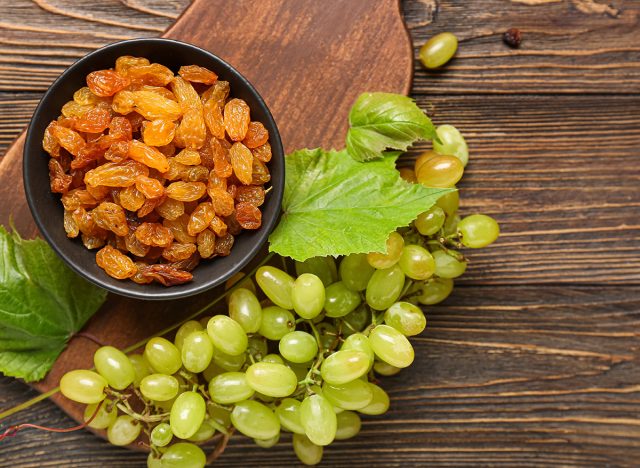 Bowl with tasty raisins and ripe grapes on wooden background