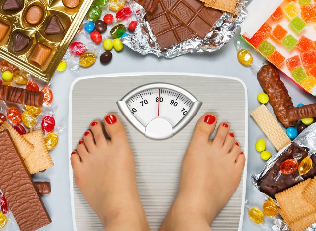 Unhealthy diet - overweight. Feet on bathroom scale and chocolate, jelly cubes, candies, chocolate bars, cookies, donuts