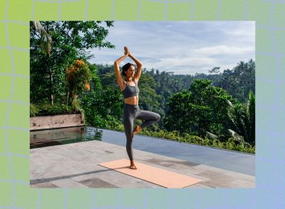 fit woman doing tree pose exercise on yoga mat outdoors on deck overlooking lush foliage and an infinity pool