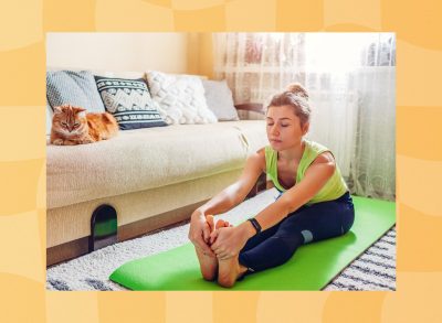 woman doing forward fold stretch on green yoga mat in bright living space