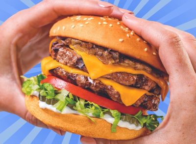 The Double Char from Habit Burger Grill held by two hands, set against a colorful blue background