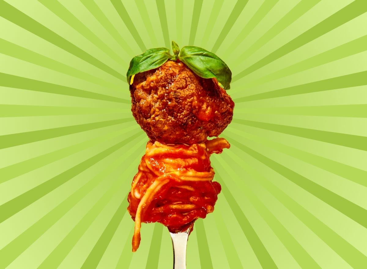 Saucy spaghetti twirled around a fork with a meatball on top, set against a vibrant green background