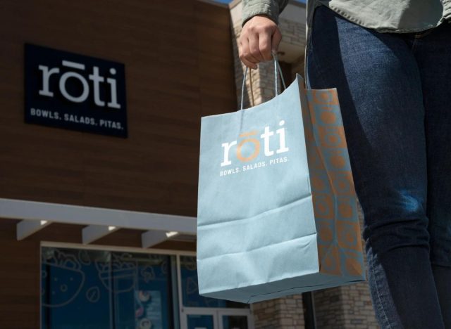 Roti customer holding a bag of food in front of the store