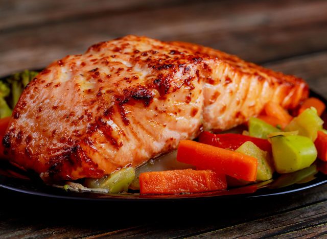 Baked juicy salmon fillet with steamed vegetables on black plate