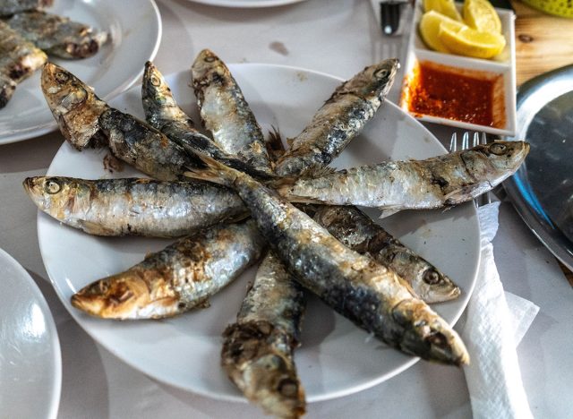 Fried sardines on a plate with lemon wedges, sauce, and sides.